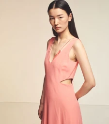 Model Houjing Cui poses in a sleeveless peach pink cutout dress against an off-white seamless studio backdrop.