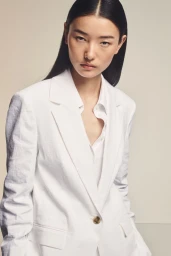 Model Houjing Cui wearing an oversized white tailored blazer and white shirt against a neutral studio backdrop.