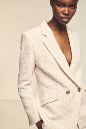 Model Elvina Patrick posing in a tailored double-breasted cream tweed blazer against a neutral studio backdrop for BOSS.