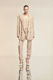 Model standing on a reflective surface wearing a beige pinstripe suit and blazer for the BOSS Spring Summer 2024 campaign.