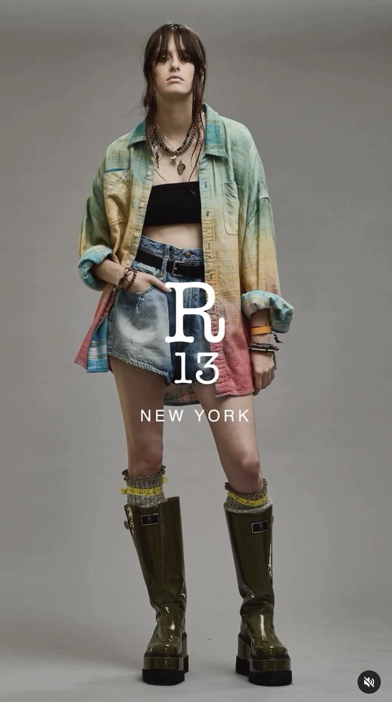 Fashion editorial shot of a female model wearing a tie-dye shirt, denim shorts, platform boots, and jewelry, set against a neutral backdrop.