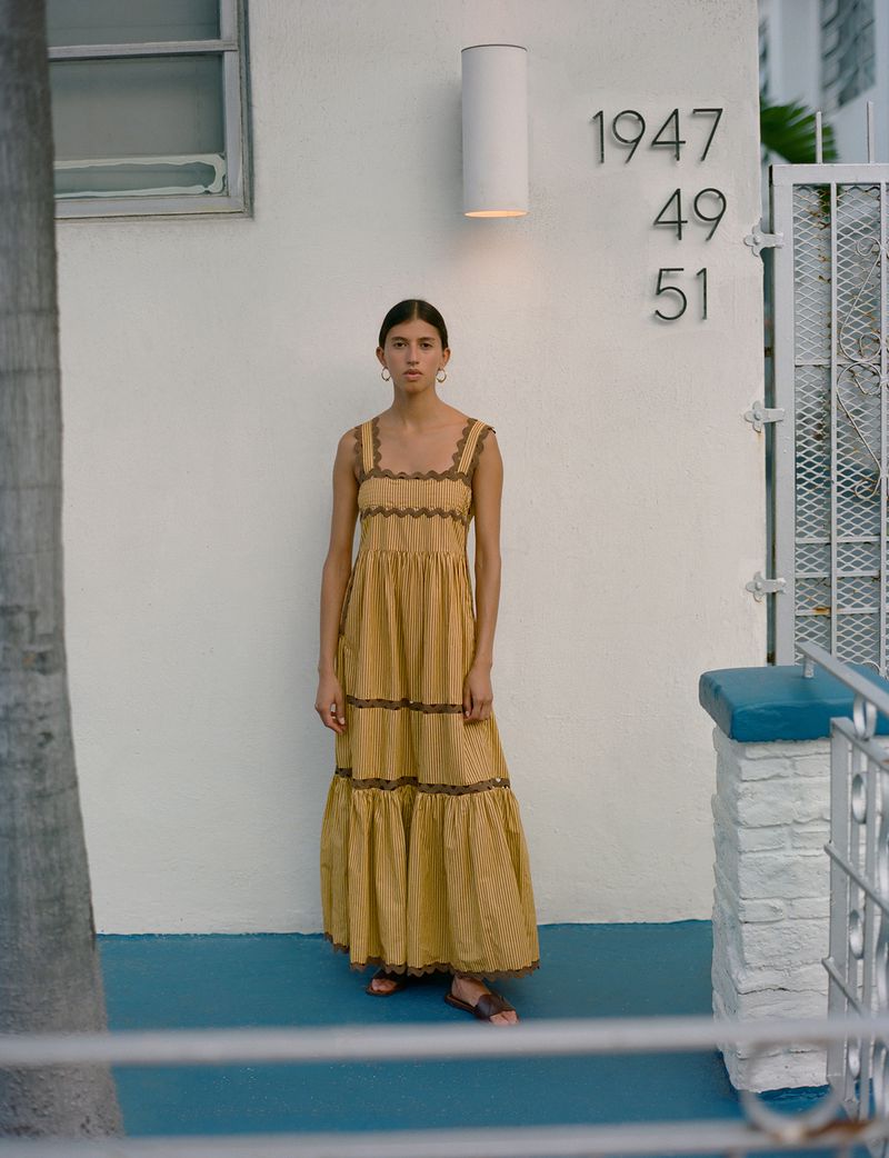 Woman in a yellow dress stands outside a building with address numbers 1947, 49, and 51 on a white wall in an urban setting.
