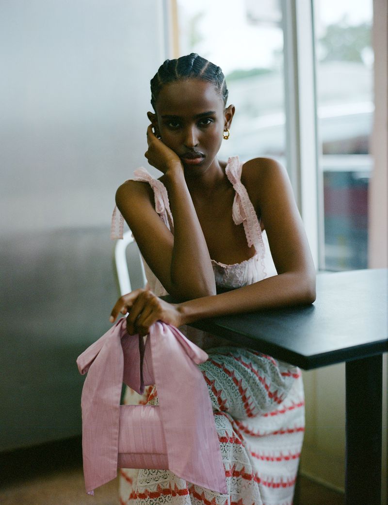 Portrait of a slender African American woman in a pink dress, seated at a table, holding a pink purse, looking directly at the camera.