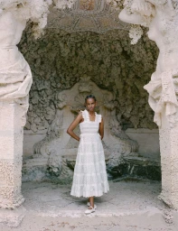 Model wearing a white lace dress standing framed by ornate stone architectural sculptures for Loeffler Randall