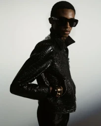 Model wearing black crocodile-embossed jacket and oversized sunglasses against a neutral background