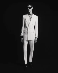 Model wearing a white double-breasted suit and sunglasses against a solid black background for Tom Ford