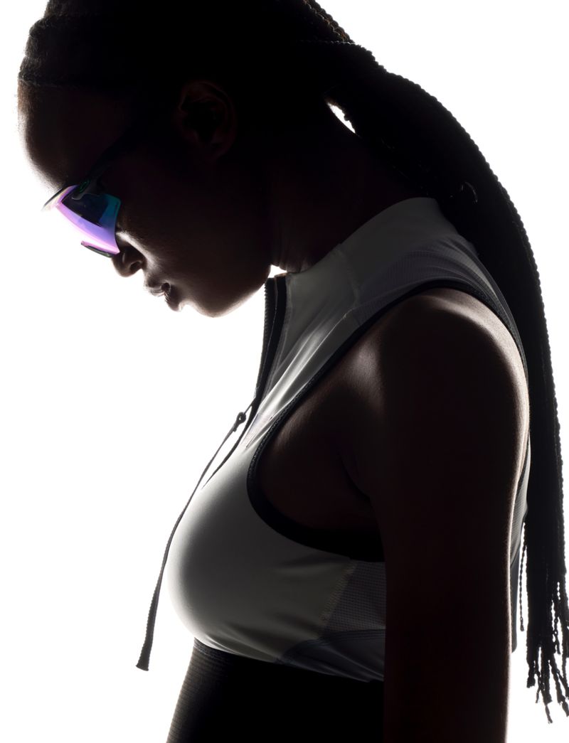 Silhouette portrait of a woman with braided hair wearing sport sunglasses and a sleeveless top against a bright white background.