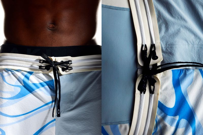Torso of a dark-skinned adult male wearing patterned blue and white swim trunks with a drawstring closure in a studio setting.