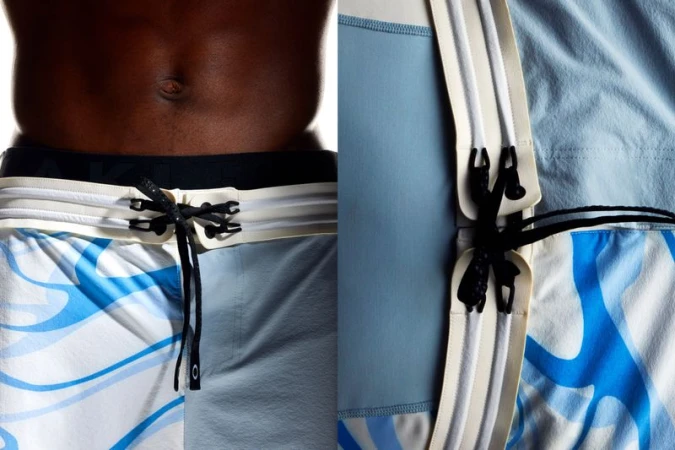Torso of a dark-skinned adult male wearing patterned blue and white swim trunks with a drawstring closure in a studio setting.