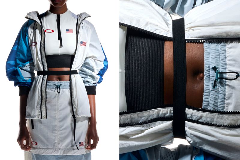 Model presents athletic-style jacket and skirt with visible skin, indoors under soft light, featuring zippers, straps, and patriotic patches.