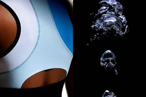 Close-up of an athlete's back in a blue and white performance top alongside water bubbles against a black background.