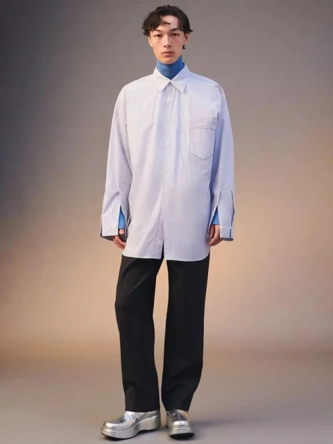 Full-length shot of an Asian man in an oversized striped shirt, black pants, and silver platform shoes, set against a gradient background.