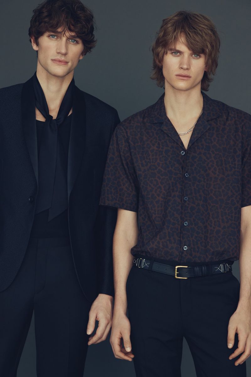 Two male models posing in tailored black formalwear and a patterned button-up shirt against a studio backdrop.