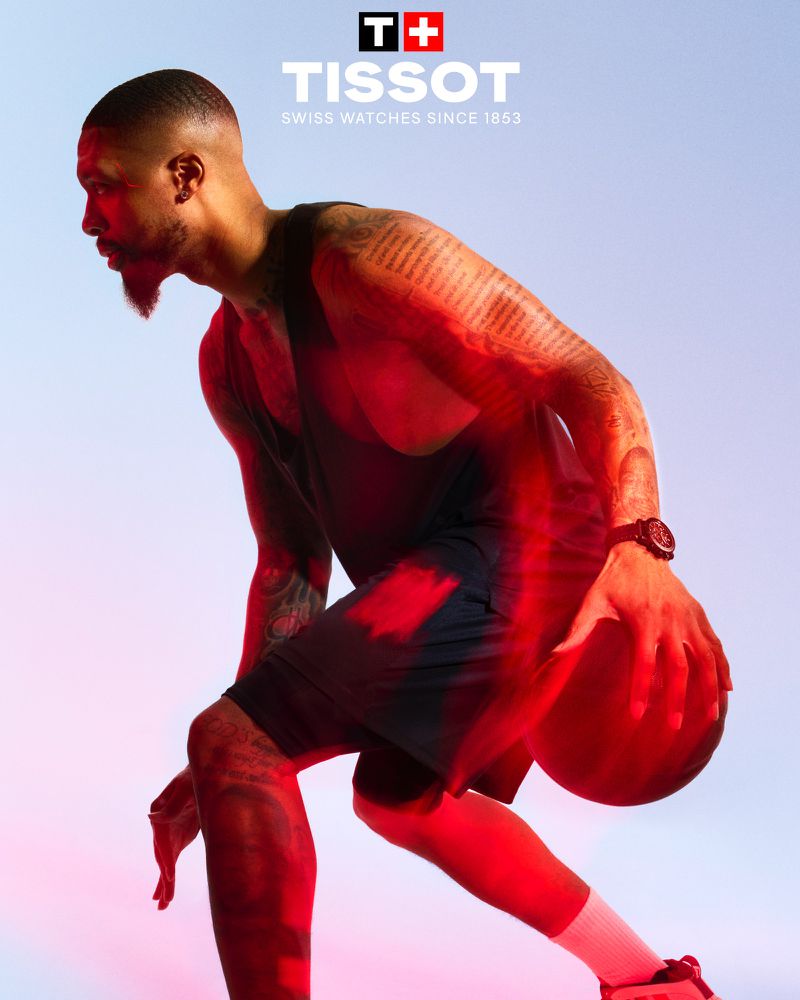 Male basketball player in action, wearing a tank top and shorts, dribbling a ball in a studio with red and blue lighting.