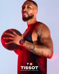 Damian Lillard holding a basketball and wearing a black Tissot wristwatch under dramatic red studio lighting.