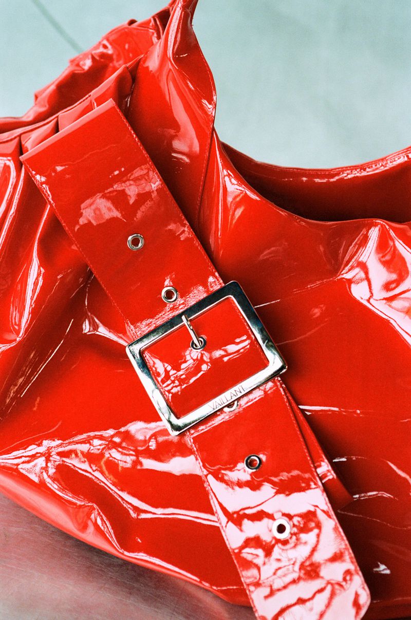 Close-up of a glossy, bright red patent leather handbag with a silver-buckled red strap, showcasing fashion accessory details.