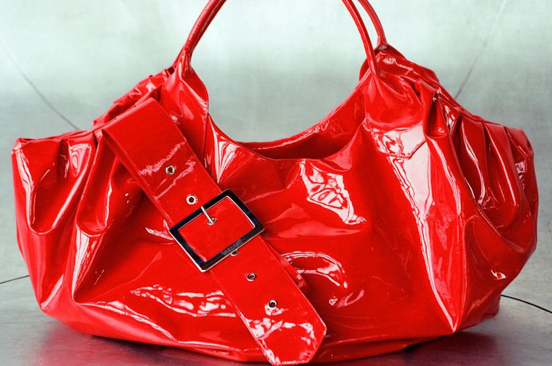 Red patent leather handbag with a silver buckle, showcasing a shiny and eye-catching accessory against a neutral backdrop.