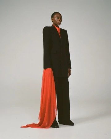 An adult woman in a black suit and red scarf poses in a photo studio with a full shot on a white background. Fashion editorial.