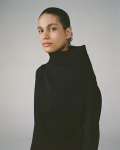Model wearing a black sculptural high-neck draped top against a neutral studio backdrop for Alain Paul SS24.