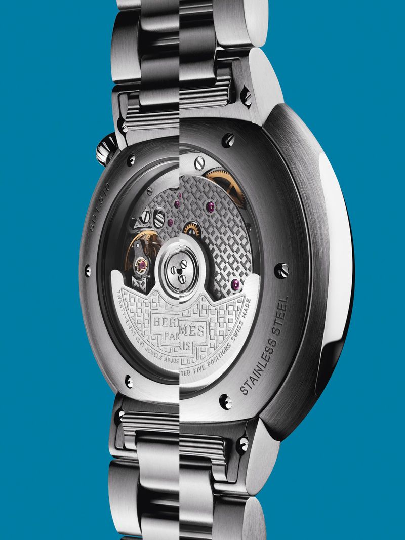 Silver stainless steel wristwatch with an exposed mechanical movement on a blue background in a studio product shot. 