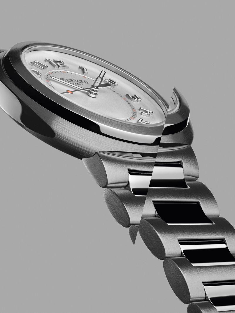 Wristwatch with a metal band and round silver face with numerical hour markers and silver hands is photographed in a close-up studio shot.