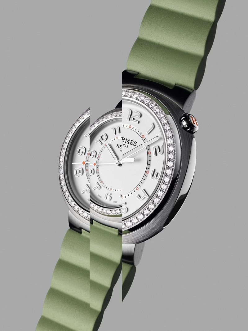 Elegant stainless steel and diamond-encrusted Hermès watch with a light green strap, presented against a sleek gray background.
