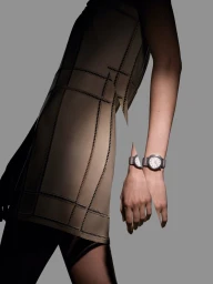 Close-up of a person wearing a luxury Hermès watch and structured beige dress against a neutral grey studio backdrop.