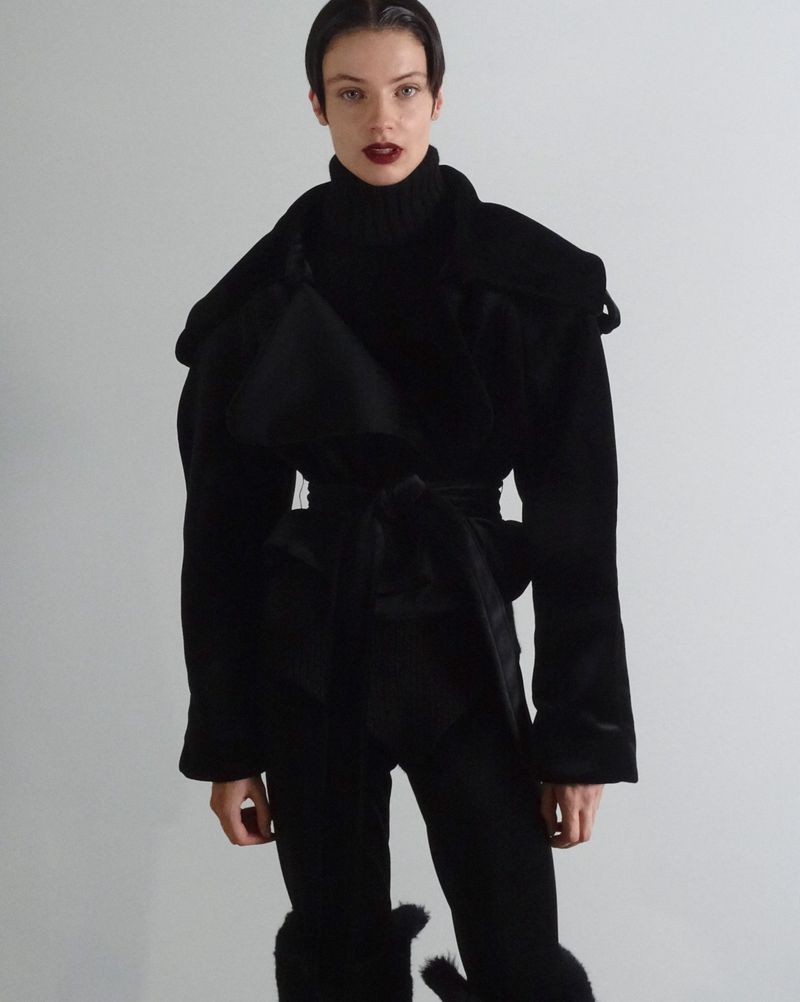 Fashionable woman in a black outfit strikes a pose against a gray backdrop, showcasing an elegant and modern design.
