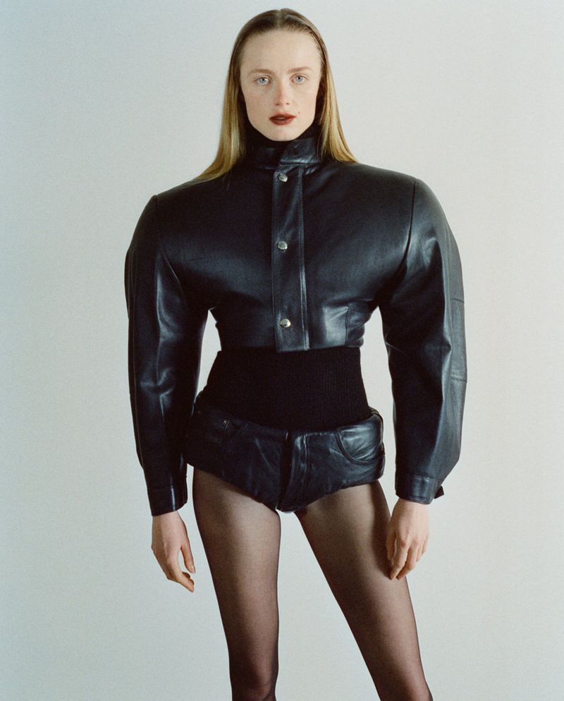 Model Rianne Van Rompaey posing in a padded black leather jacket and sculpted briefs against a clean studio background.