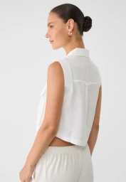 Model in profile wearing a white sleeveless collared shirt against a white backdrop