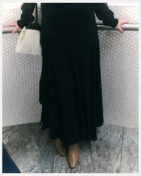 Model wearing a long black dress and tan boots holding a white handbag against white hexagon tile