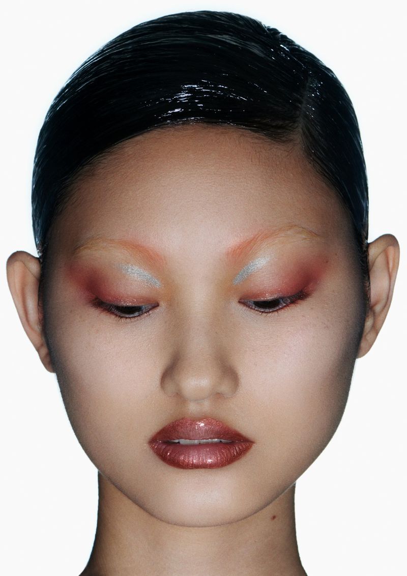 Close-up beauty shot of an Asian adult female model showcasing colorful makeup on her eyes and glossy lips against a bright white background.
