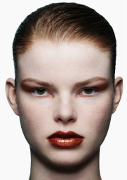 Close-up beauty portrait of a woman with slicked-back auburn hair, glossy copper lipstick, and warm eyeshadow against a white background.
