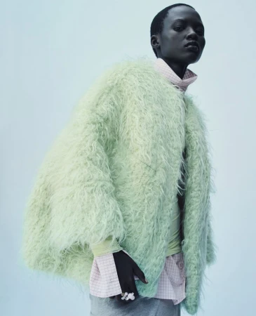 Model in an oversized mint green shaggy textured coat layered over a pink checkered shirt against a pale cool backdrop.