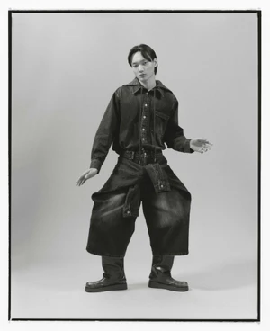 Model wearing an oversized denim shirt, sculptural wide-leg culottes, and chunky boots against a grey studio backdrop for Goomheo AW24.