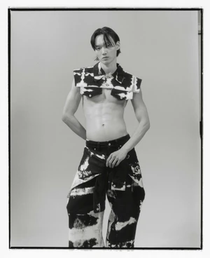 East Asian male model posing shirtless in a cropped patterned collar jacket and matching wide-leg trousers against a studio backdrop.