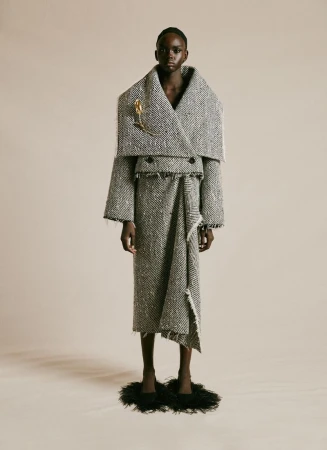 A full-length portrait of a Black female fashion model wearing an oversized grey and white tweed suit with an A-line skirt and feather shoes.