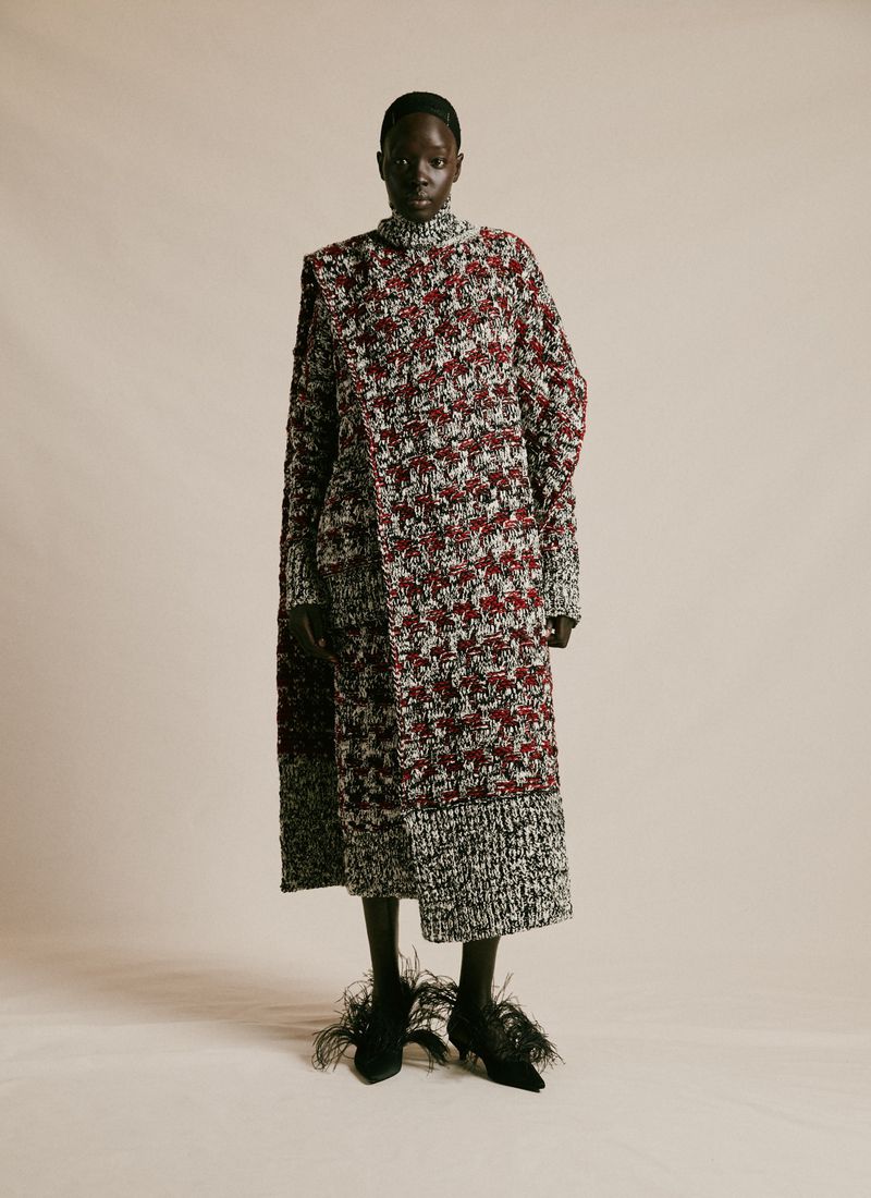 Full-length portrait of a Black woman in a textured long-sleeved dress with feathered heels, against a neutral studio backdrop.