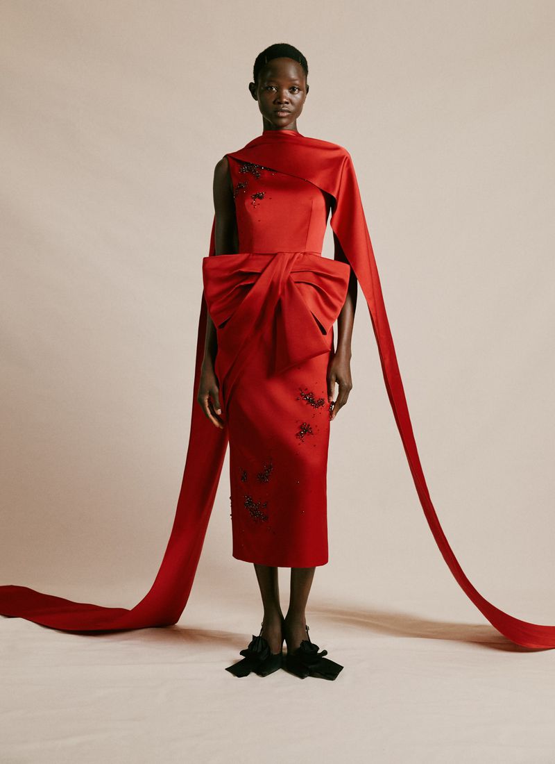 Elegant Black woman poses in a fitted, sleeveless red dress with long ribbon accents, emphasizing its stylish bow and modern design.