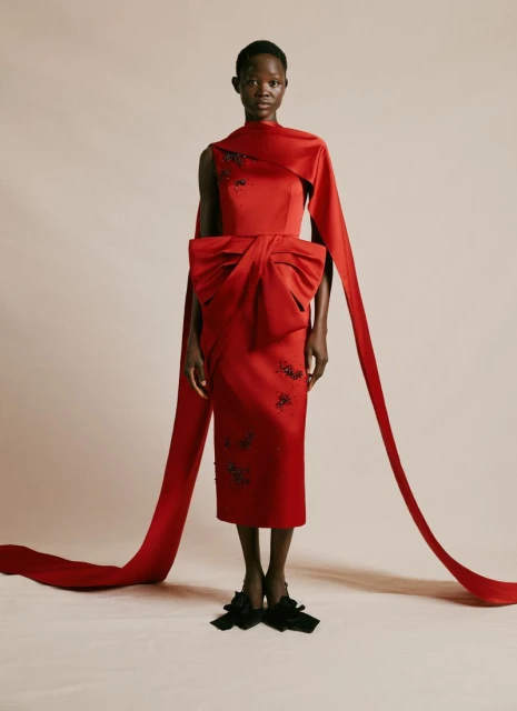 Elegant Black woman poses in a fitted, sleeveless red dress with long ribbon accents, emphasizing its stylish bow and modern design.