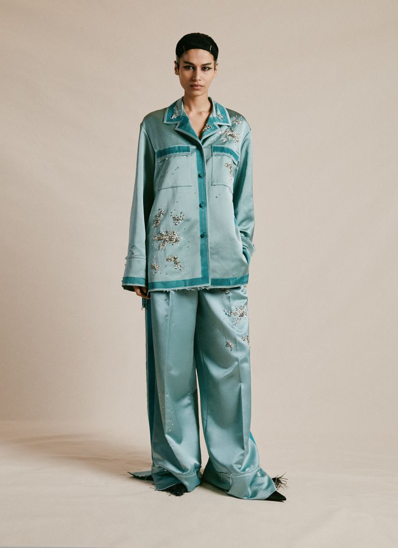 Elegant adult female wearing matching teal pajama set with floral embroidery in a full shot in a neutral setting, fashion concept.