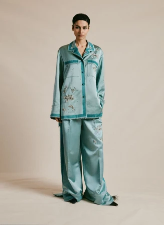 Elegant adult female wearing matching teal pajama set with floral embroidery in a full shot in a neutral setting, fashion concept.