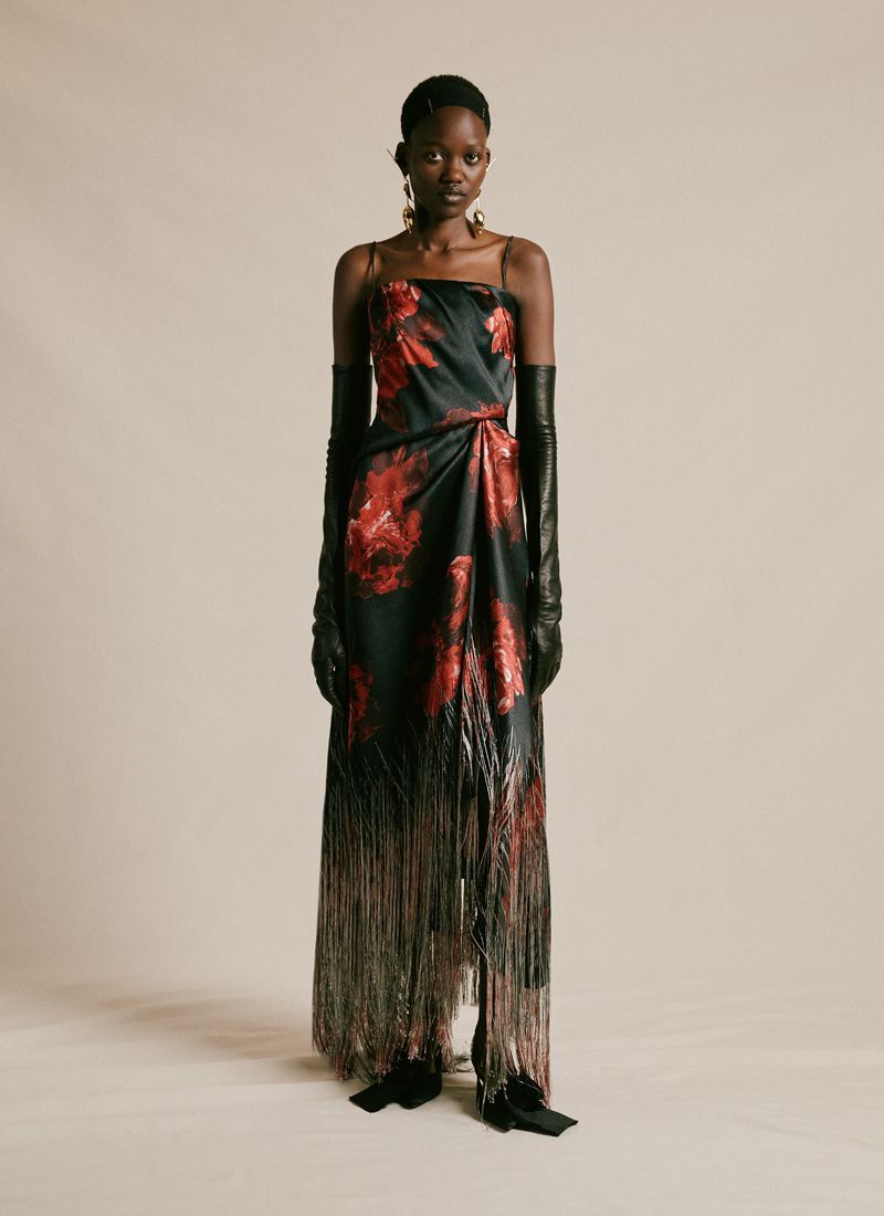 A single Black female fashion model poses in a sleeveless, floor-length gown with floral patterns, long gloves, and dangling earrings.