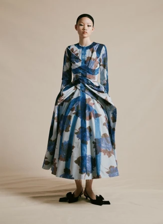 Asian woman in a full-length portrait wearing a blue and beige floral print dress and black heels in a neutral studio setting.