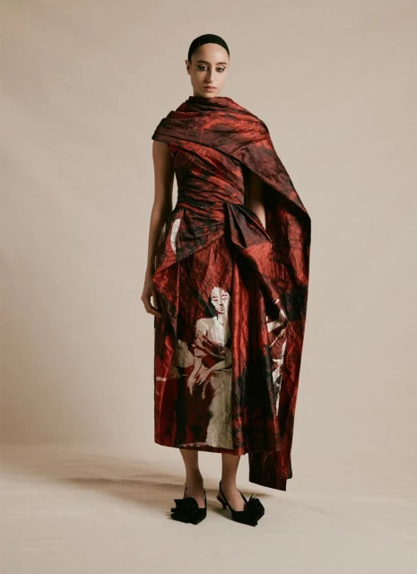 Woman in a red and black printed dress and black heels stands in a neutral studio, fashionable and artful in a full-length shot.