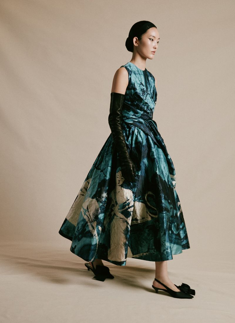 Elegant woman in a teal and ivory full-length dress with black opera gloves and slingback heels poses in a neutral studio setting.