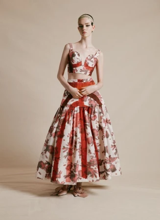 Fashion model poses in studio wearing floral crop top and skirt ensemble with brown accents on a neutral background in portrait orientation.
