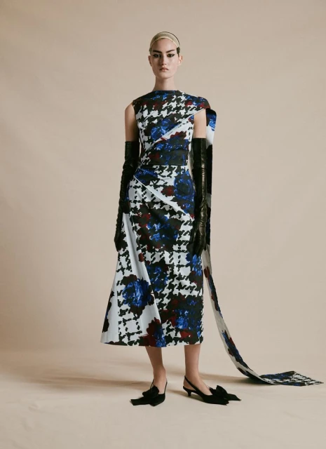 Fashion model posing in a black, white, and blue houndstooth dress with matching train and black gloves and heels on a beige background.