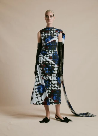 Fashion model posing in a black, white, and blue houndstooth dress with matching train and black gloves and heels on a beige background.