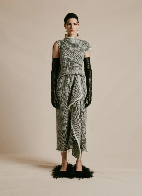 Full-length shot of a woman in a textured gray dress with fringe, styled with opera gloves and black feather shoes, in a studio setting.